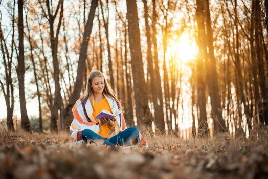 Young girl reading a book in bright colorful forest and breathing fresh air
