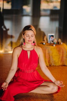 Meditation and concentration. a woman in a red dress, sitting on the floor with her eyes closed, is practicing medicine indoors. Peace and relaxation.