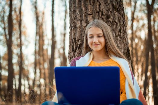 Beautiful smiling female working on the laptop outdoors in an Autumn park