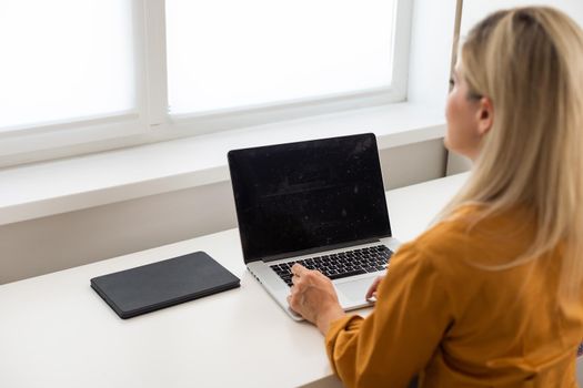 Mockup image of a woman using and typing on laptop with blank white desktop screen on wooden table