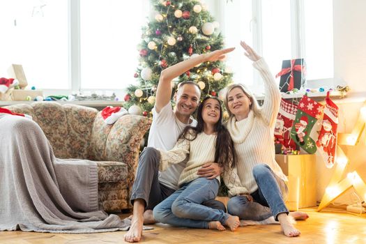 Beautiful young family enjoying their holiday time together, decorating Christmas tree, arranging the christmas lights and having fun