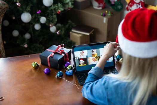 A young woman on the background of a Christmas tree with gifts, with a tablet has a video call or video chat with friends, family. Christmas online holiday. Stay home vacation.