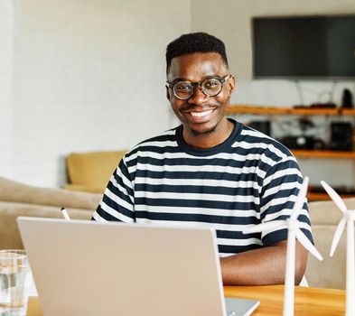 Portrait of a young black man using laptop and looking at windmill models at home