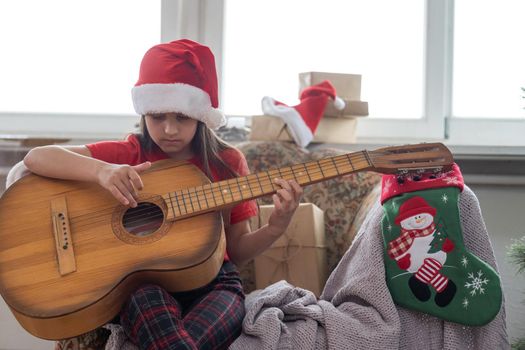 Happy little girl in red hat playing the on the background of christmas tree. Talent kid having fun on winter holidays at cozy decorated home