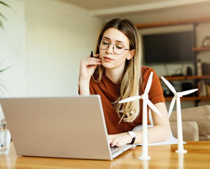 Portrait of a young girl using laptop and looking at windmill models at home