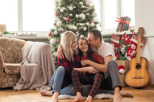 Happy family with cute daughter near Christmas tree together at home.