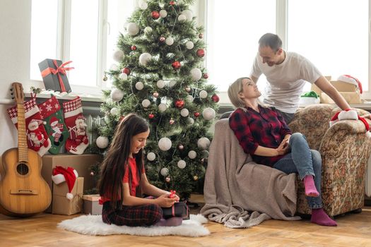 Happy family with cute daughter near Christmas tree together at home.