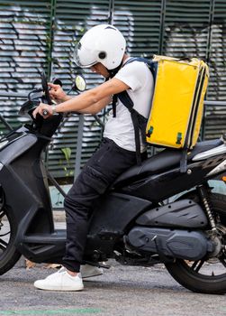 Young courier, delivery man searching his destination path on the mobile , with thermo backpack on a moped on a street. Fast transport express home delivery. Online order