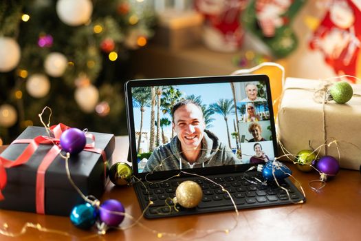 Family video call with kid presenting gift by remote chat digital tablet screen on Merry Christmas table holiday background. Xmas online virtual family party celebration, Happy New Year videocall.