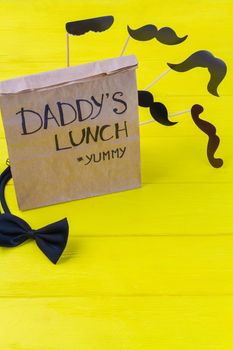 Paper bag with bow tie on yellow wooden desk. Vertical shot top view copy space.