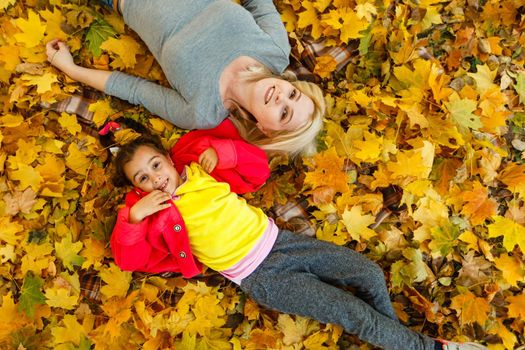 mother and daughter lying on the leaves at the autumn park