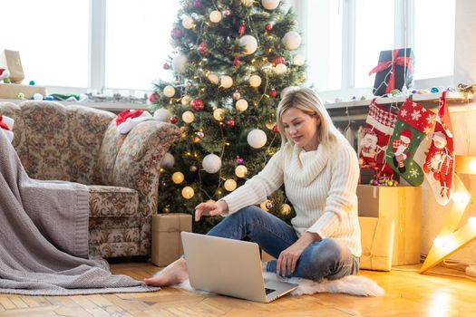 Young woman works at home remotely with laptop on the background of a Christmas tree. Quarantine, work on holidays. atmosphere and work at home