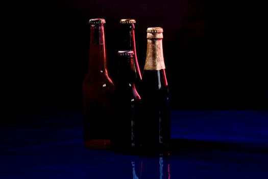 silhouettes of four beer bottles on a black background, placed on a blue shiny surface..