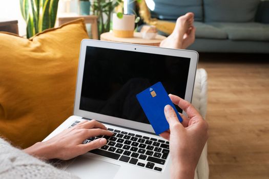 POV of young caucasian woman shopping online with credit card using laptop at home cozy living room. Copy space. E-commerce concept.