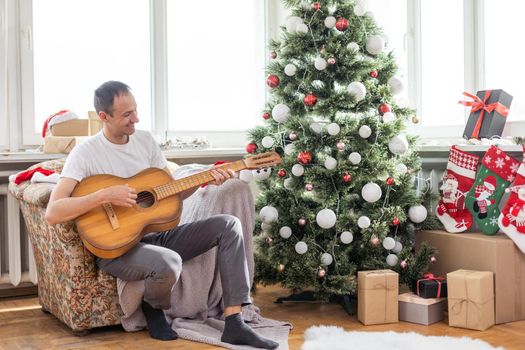 young handsome man sitting on the sofa, he is playing guitar, music, christmas, relax concept.