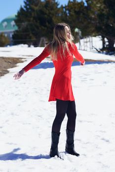 Young blonde woman wearing a red dress and black stockings opening her arms in happiness in the snowy mountains, in Sierra Nevada, Granada, Spain.