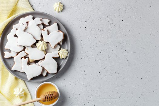 Easter cookies in the form of a rabbit on a gray plate with honey and yellow textiles on a gray background. copy space