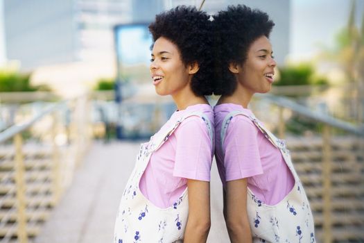 Side view of delighted African American female looking into distance while standing near glass building in city against blurred background