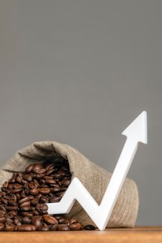 A bag of coffee beans and a chart arrow pointing up. The cost of coffee in the markets of the world. The concept of the growth of the cost of coffee beans.