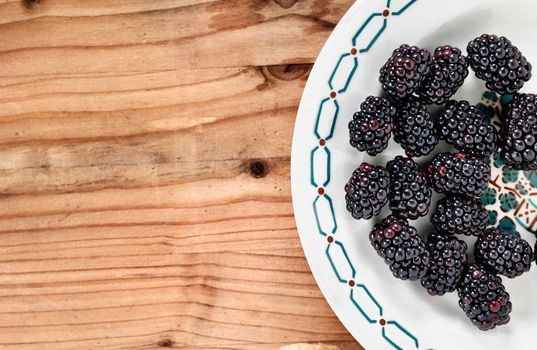 Fresh wild blackberries on white plate on wooden table , edible fruit