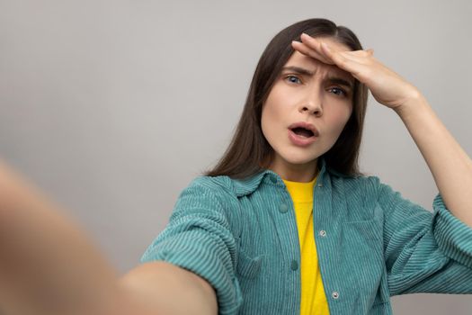 Portrait of astonished woman with amazed face expression, making selfie, looking far away, point of view photo, wearing casual style jacket. Indoor studio shot isolated on gray background.