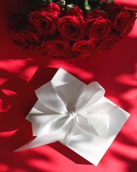 Happy holidays, luxe shopping and love gifts concept - Luxury holiday silk gift box and bouquet of roses on red background, romantic surprise and flowers as birthday or Valentines Day present