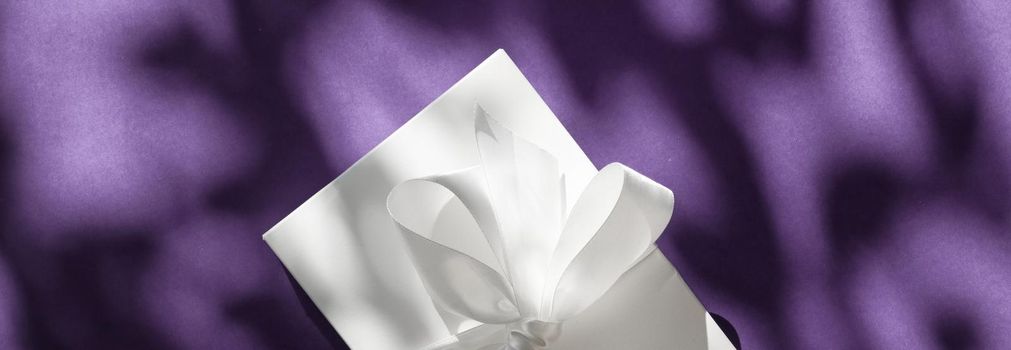 Anniversary celebration, shop sale promotion and bridal surprise concept - Luxury holiday white gift box with silk ribbon and bow on violet background, luxe wedding or birthday present