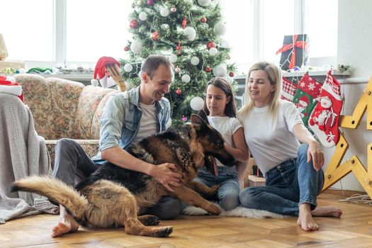 Excited girl and her family sitting on the floor near christmas tree and smiling. family during Christmastime.