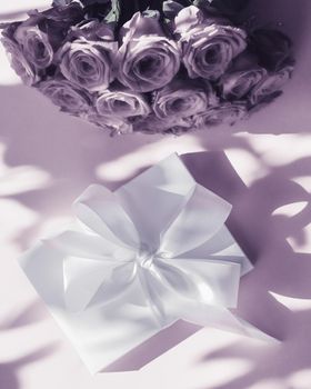 Happy holidays, luxe shopping and love gifts concept - Luxury holiday silk gift box and bouquet of roses on purple background, romantic surprise and flowers as birthday or Valentines Day present