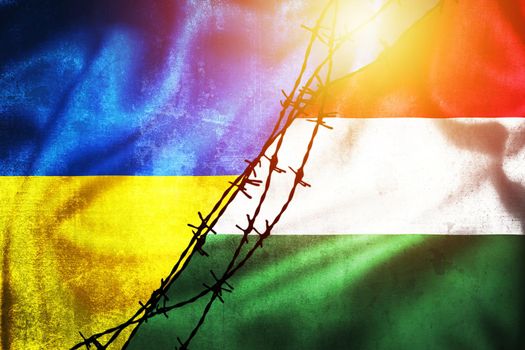 Grunge flags of Ukraine and Hungary divided by barb wire illustration sun haze view, concept of tense relations between two countries