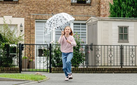 Preteen girl running with umbrella outdoors. Pretty child kid portrait in rainy day at street