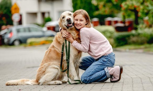 Preteen girl with golden retriever dog sitting outdoors together and looking at camera. Pretty kid child with purebred pet doggy at street