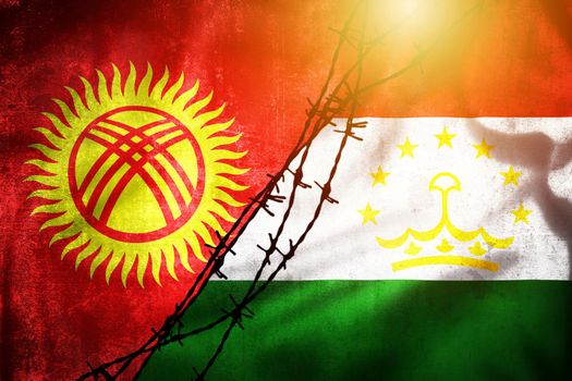 Grunge flags of Kyrgyzstan and Tajikistan divided by barb wire illustration sun haze view, concept of tense relations between two countries