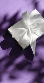 Anniversary celebration, shop sale promotion and bridal surprise concept - Luxury holiday white gift box with silk ribbon and bow on violet background, luxe wedding or birthday present