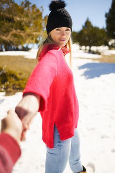 Blonde woman in winter clothes walking holding her partner's hand in the snowy mountains., in Sierra Nevada, Granada, Spain.