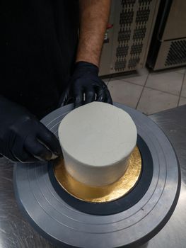 Decorator using spatula and scraper to smooth buttercream on a frosted cake