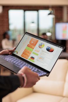 Man holding laptop with business charts in company office, management presentation of diagrams and graphs on computer screen. Data report and research information on pc. Close up.