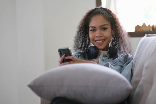Young relaxed woman listening to the music resting on the sofa at home. Caucasian girl using smart phone and headphones for music application online..