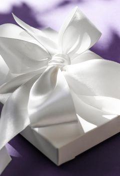 Anniversary celebration, shop sale promotion and bridal surprise concept - Luxury holiday white gift box with silk ribbon and bow on violet background, luxe wedding or birthday present