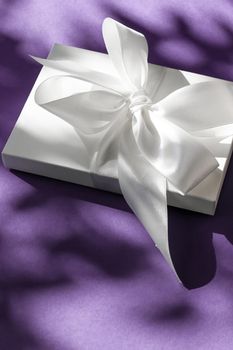 Anniversary celebration, shop sale promotion and bridal surprise concept - Luxury holiday white gift box with silk ribbon and bow on violet background, luxe wedding or birthday present