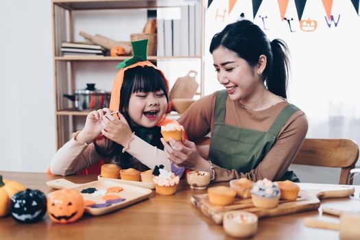 Young girl and mother at Halloween making treats and cupcake on table. Happy Halloween day.