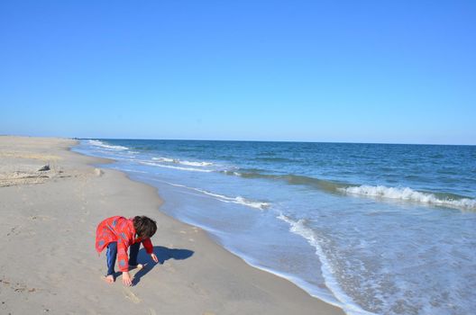 boy in red jacket and beach with water and sand and waves