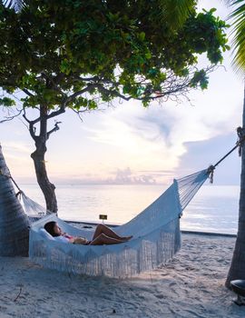 women watching sunrise in a White hammock under palm trees at a tropical beach in Thailand Hua Hin. Tropical beach in Huahin with a hammock by the ocean on a white beach