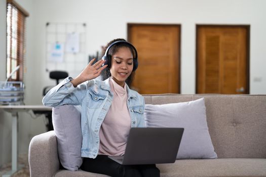 Young woman sitting on sofa at home video call chatting with friends using a laptop at home