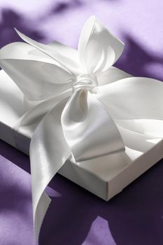 Anniversary celebration, shop sale promotion and bridal surprise concept - Luxury holiday white gift box with silk ribbon and bow on violet background, luxe wedding or birthday present