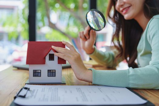 customer holding a magnifying glass to look at a house model, concept of home inspection before buying a house and land