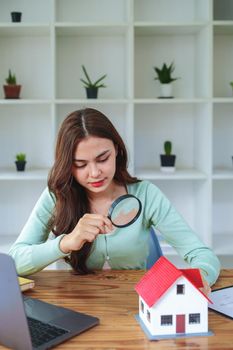 customer holding a magnifying glass to look at a house model, concept of home inspection before buying a house and land