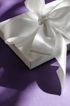 Anniversary celebration, shop sale promotion and bridal surprise concept - Luxury holiday white gift box with silk ribbon and bow on violet background, luxe wedding or birthday present