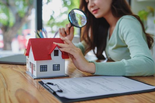 customer holding a magnifying glass to look at a house model, concept of home inspection before buying a house and land