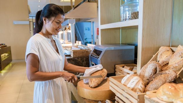 Asian woman cutting a piece of bread on a plate.